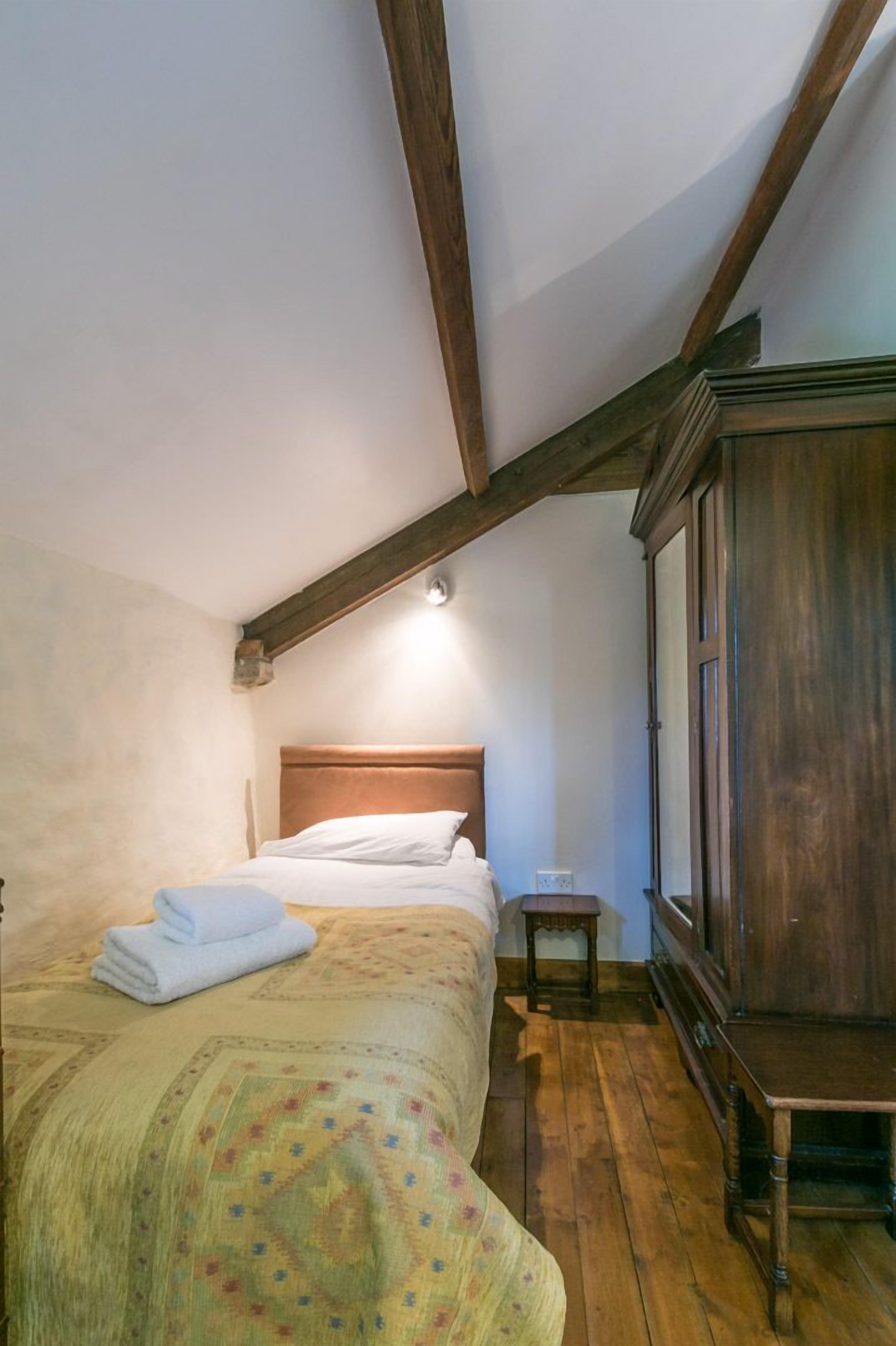 Un dormitorio con techo de madera, una cama con colcha estampada, una mesita de noche de madera y un amplio armario de madera.