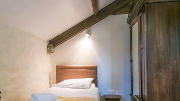 Un dormitorio con techo de madera, una cama con colcha estampada, una mesita de noche de madera y un amplio armario de madera.