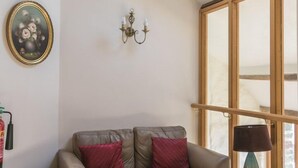 A cozy living room with a leather sofa, a small table with magazines, a wooden bench, and a skylight above. - The Barn B&B (Port Talbot)