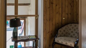 A wooden door, a chair, and a table with a lamp and books in a room with wooden beams and a window. - The Barn B&B (Port Talbot)