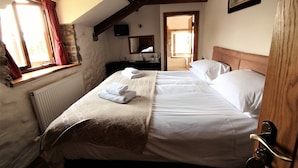 A bedroom with a bed, a window with curtains, a radiator, a wooden ceiling, and a painting on the wall. - The Barn B&B (Port Talbot)