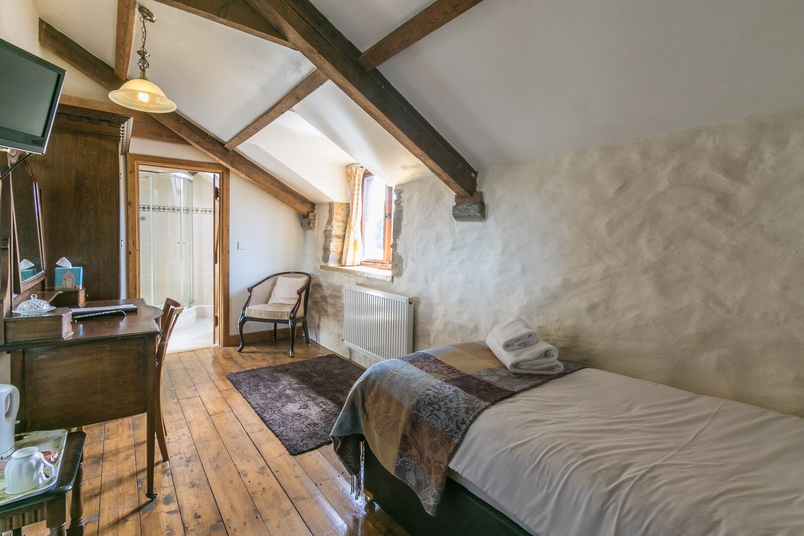 A cozy room with a wooden desk, a chair, a bed, and a window.