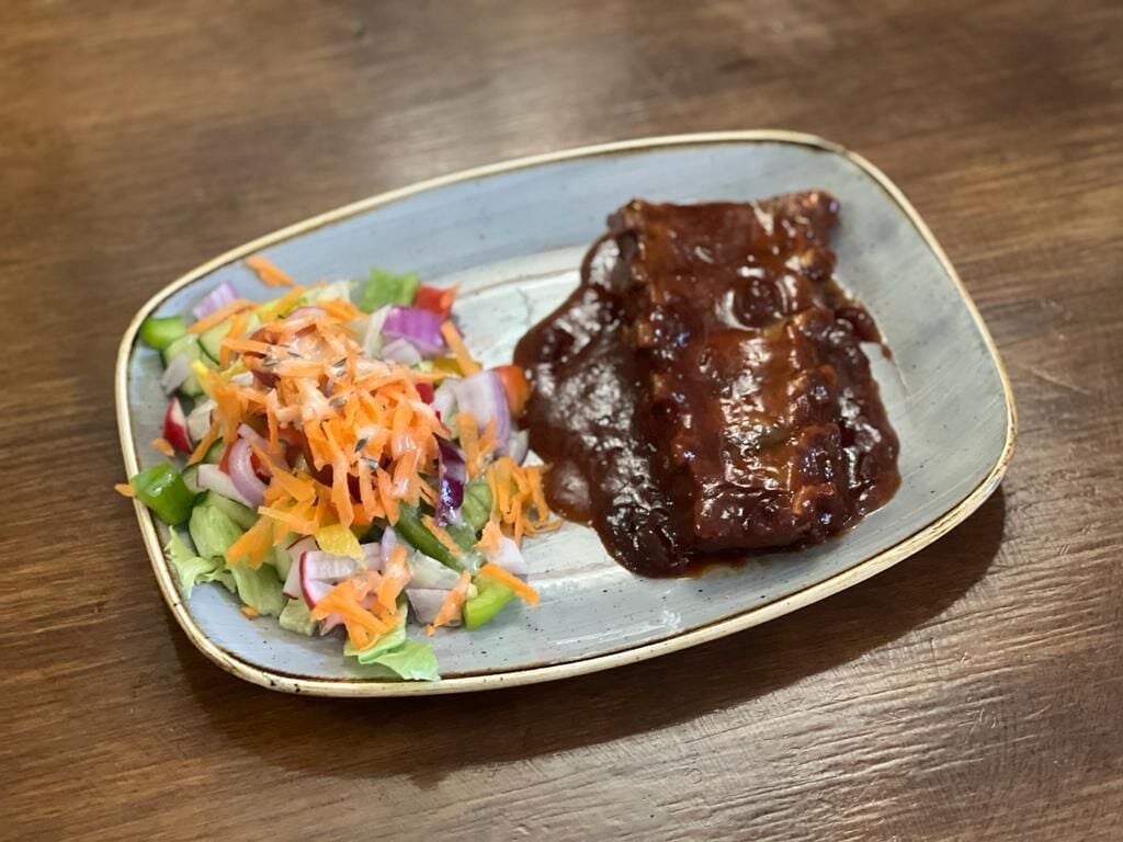 Um prato com um guisado de carne glaceado e uma salada como acompanhamento, tudo sobre um prato de cerâmica.