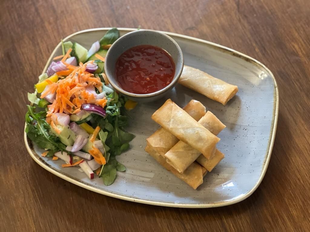 A plate with a salad and spring rolls, and a small bowl of sauce.
