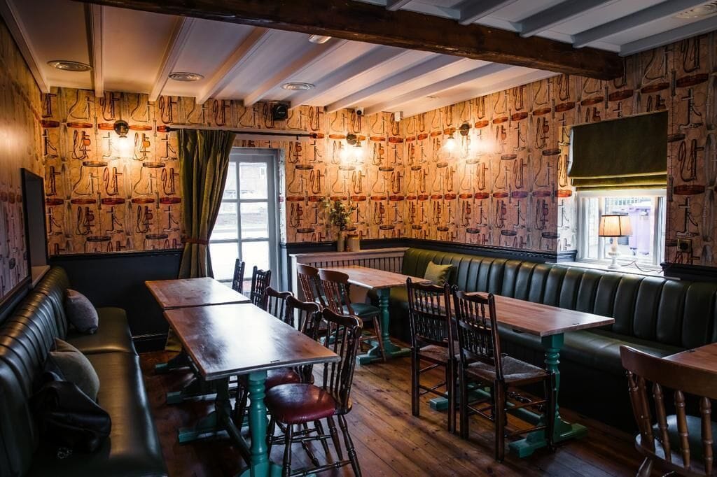 Un restaurant chaleureux avec des murs en bois, des sièges recouverts d’un tissu vert et des tables en bois.