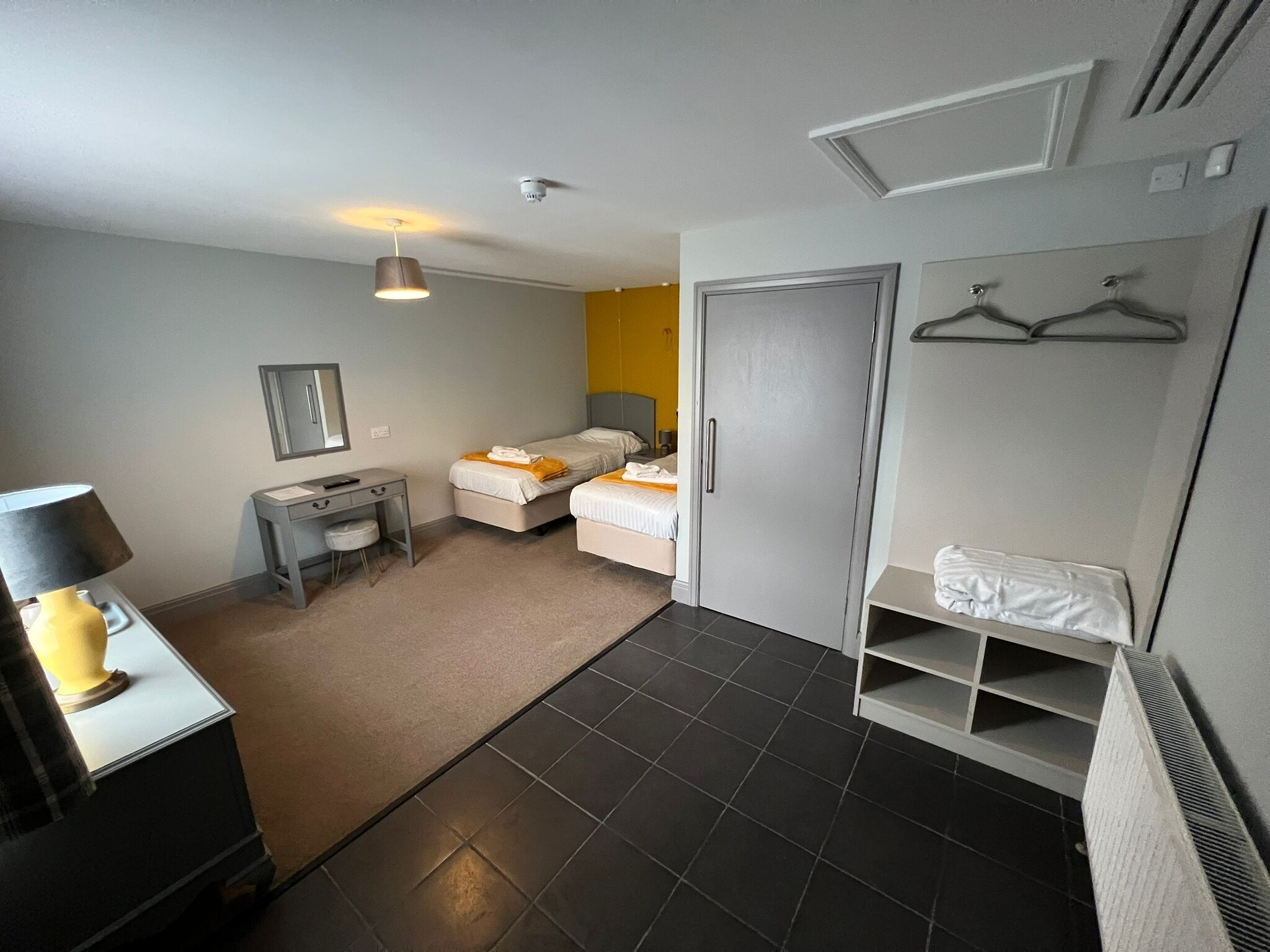A modern hotel room with two beds, a desk, a chair, a wardrobe, and a hanging coat rack.