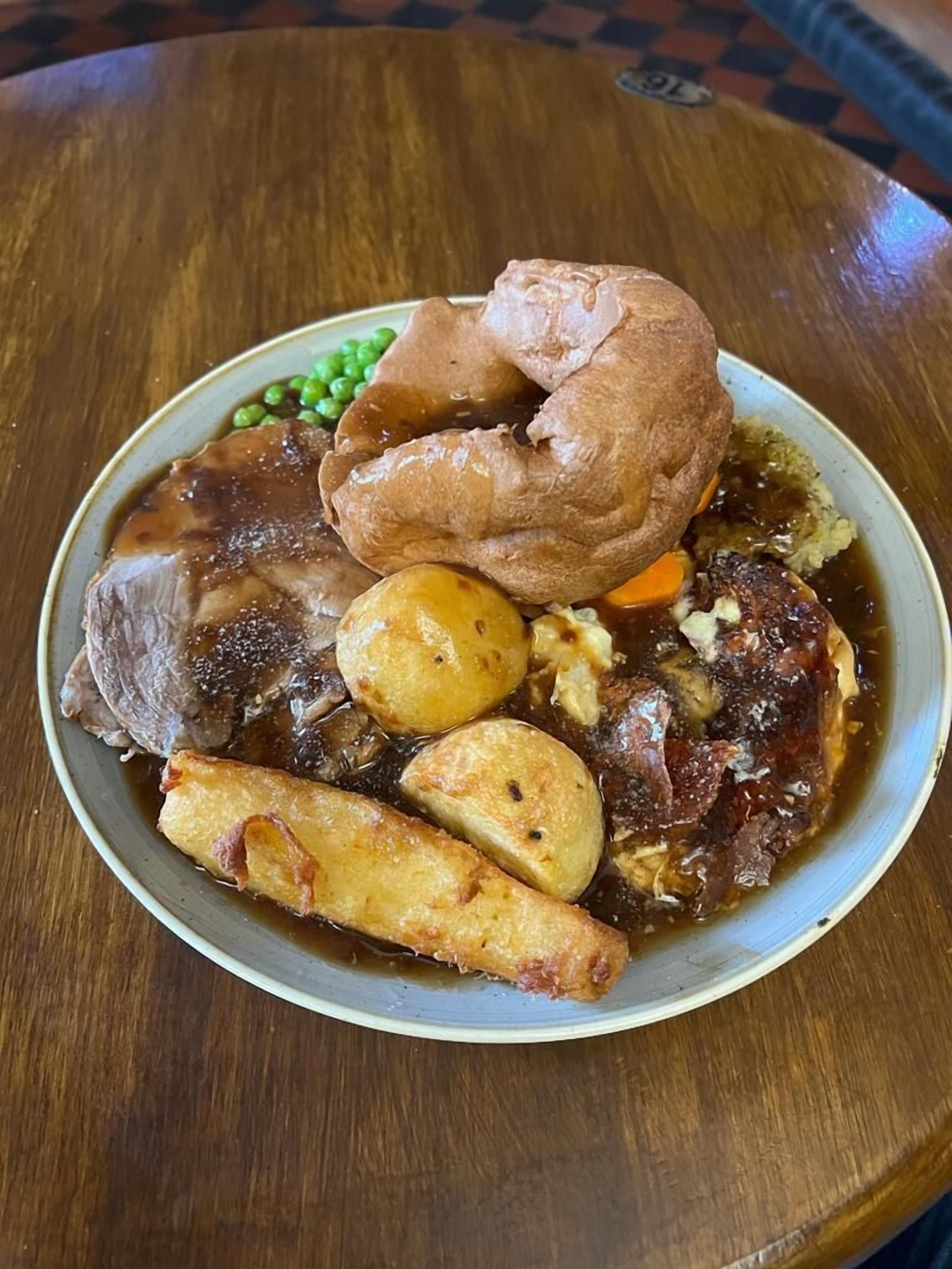 A plate of roast beef, Yorkshire pudding, peas, carrots, and Yorkshire pudding gravy.