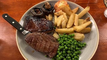 Un plato con carne, champiñones, papas fritas y guisantes.