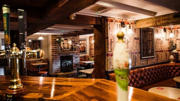 A cozy bar area with wooden flooring, a brick fireplace, and a leather booth.
