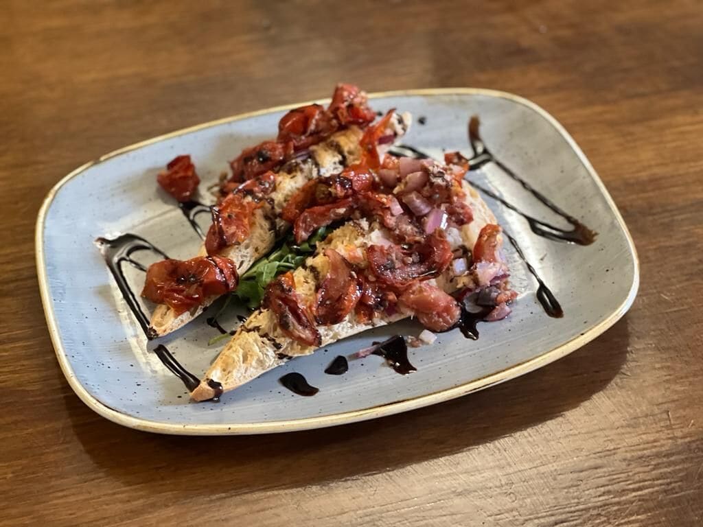 A plate with a dish topped with bacon and tomatoes, served on a ceramic plate.