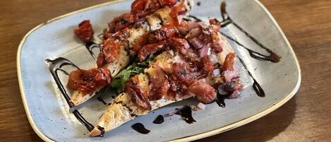 A plate with a dish topped with bacon and tomatoes, served on a ceramic plate.