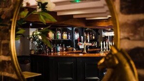 A bar area with a mirror reflecting the interior, including a shelf with various bottles and a plant.