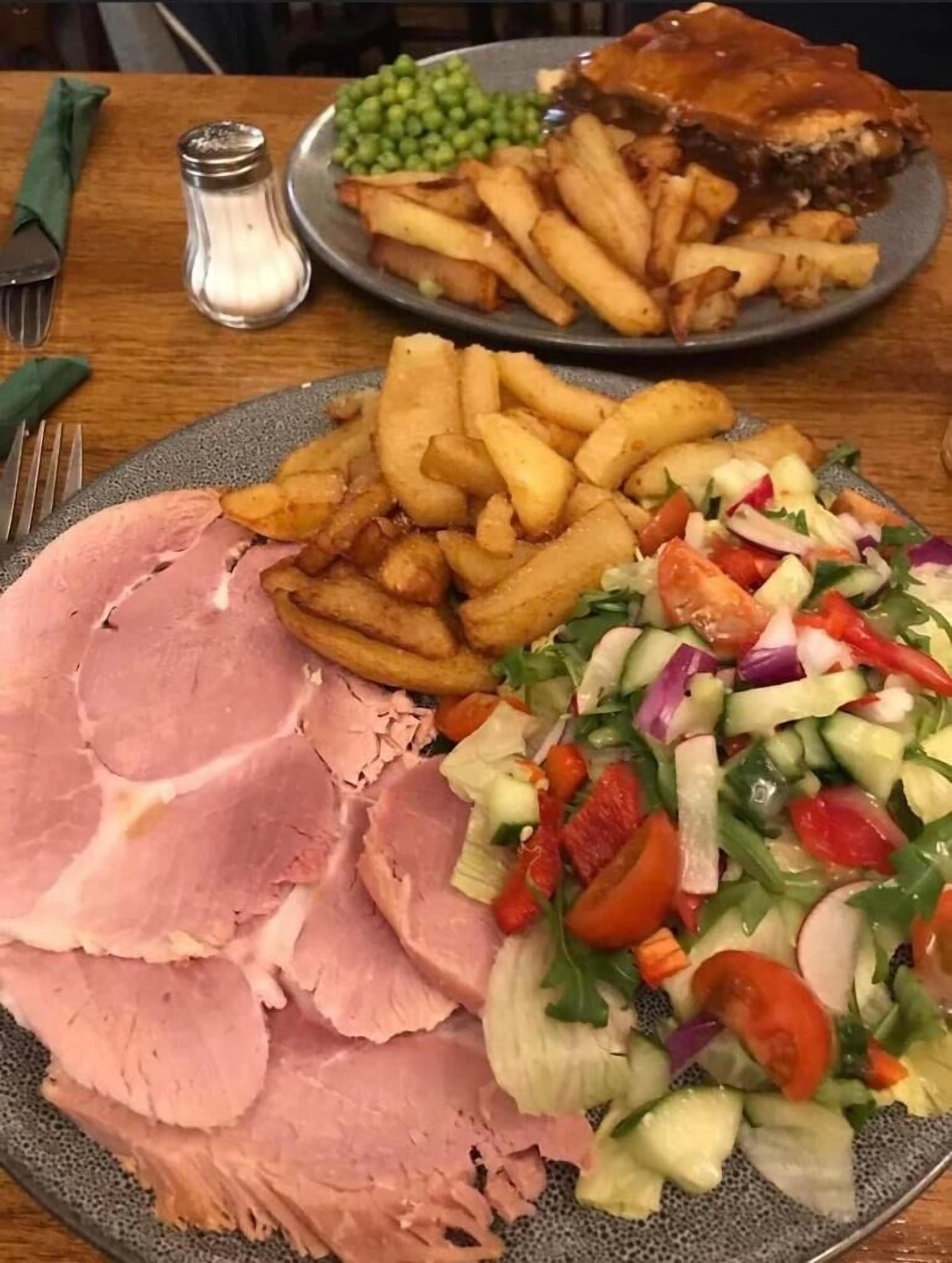 Un plato de comida con jamón, papas fritas, ensalada y un bistec.