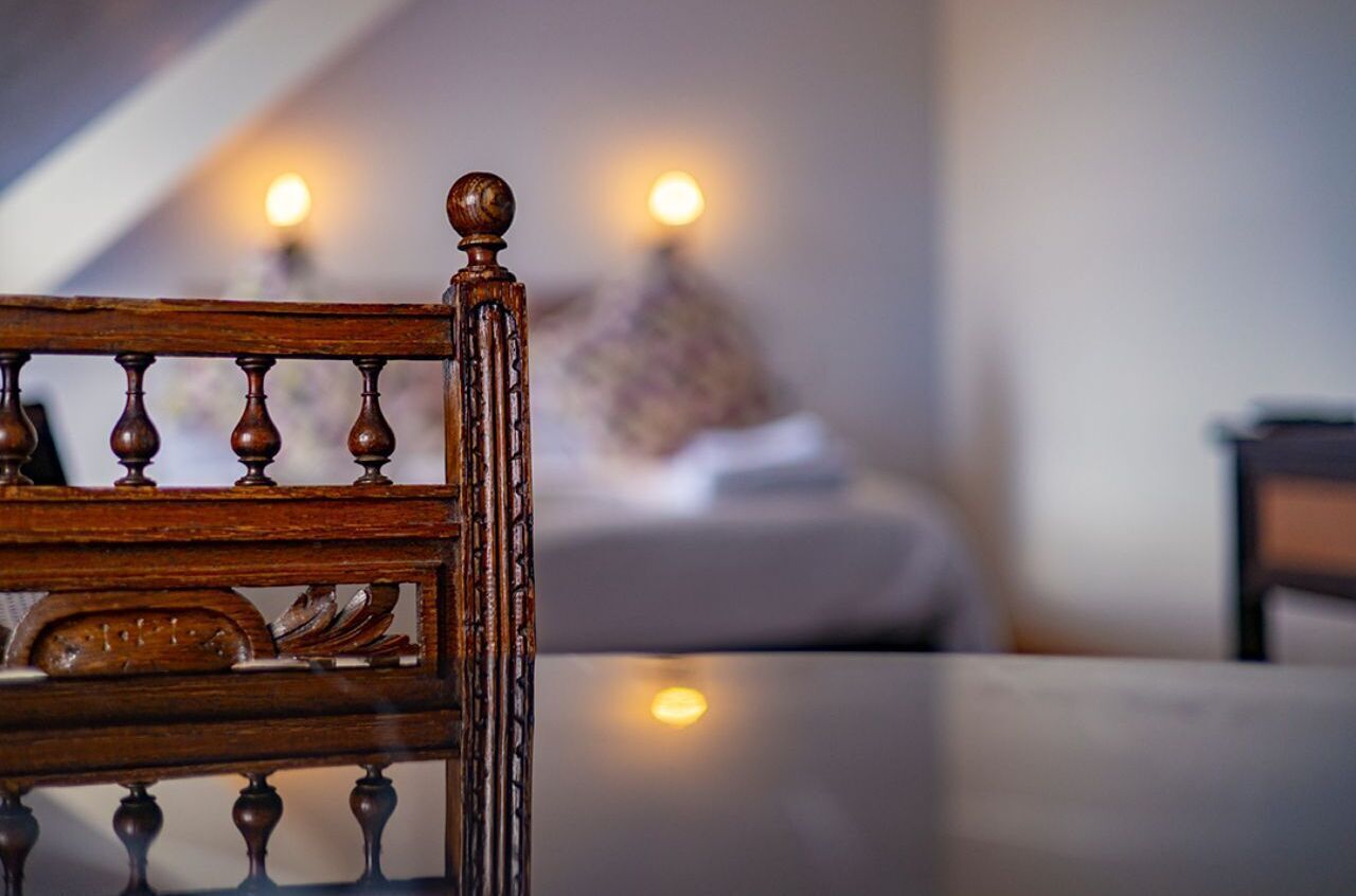 A wooden chair with a carved backrest in a room with a bed and two wall-mounted lamps.