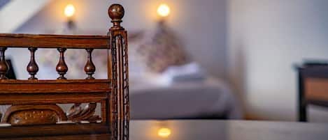 A wooden chair with a carved backrest in a room with a bed and two wall-mounted lamps.