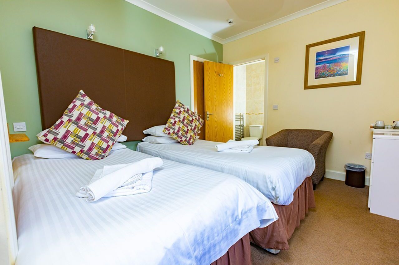 A hotel room with two beds, a chair, a desk, and a picture on the wall.