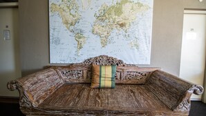 Ein Sofa aus Holz mit aufwendigen Schnitzereien, dahinter eine Weltkarte an der Wand und eine Tür mit der Nummer 21.