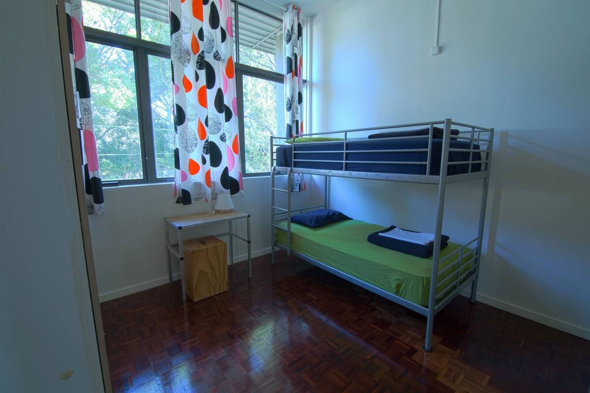 A dormitory room with a bunk bed, a desk, and a window with curtains.