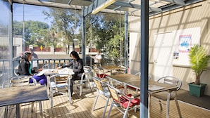 Ein Straßencafé mit Metallstühhlen und -tischen, einer Holzterrasse und einer Glaskonstruktion.