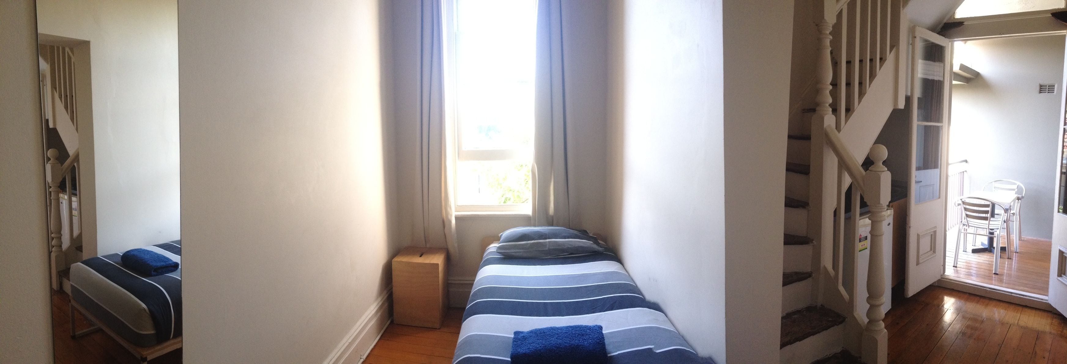 Una habitación pequeña con una cama, una mesita y una ventana.