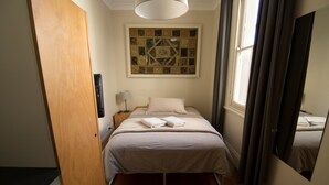 Ein Schlafzimmer mit einem Bett, einem Nachttisch, einer Lampe, einem Wandbild und einem Fenster mit Vorhängen.