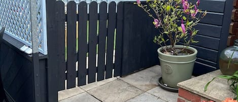 A garden area with a potted plant, a wooden fence, and a brick wall.