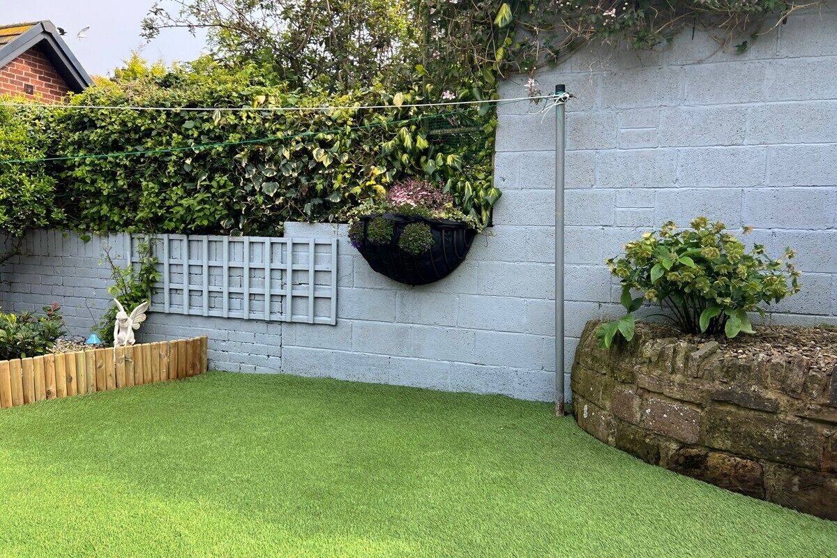 A backyard with artificial grass, a stone wall, a wooden fence, and a brick wall with climbing plants.