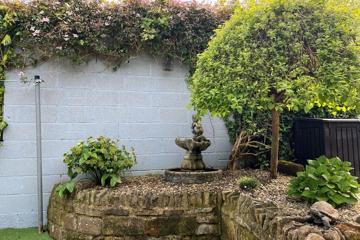 Un jardín con una fuente de piedra, un árbol y un muro.