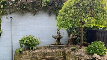 Un jardín con una fuente de piedra, un árbol y un muro.