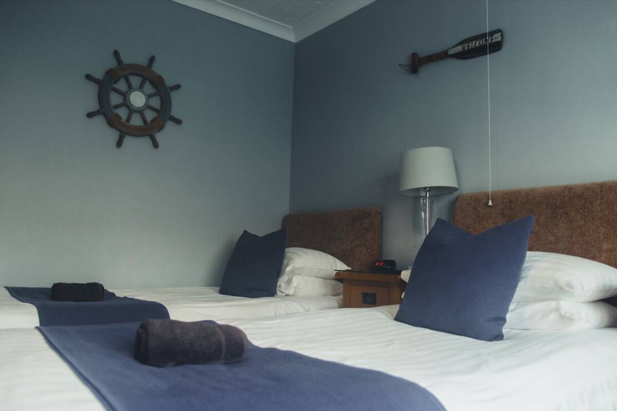 Habitación de hotel con dos camas, un adorno con forma de timón de barco, una lámpara y un bate de béisbol en la pared.