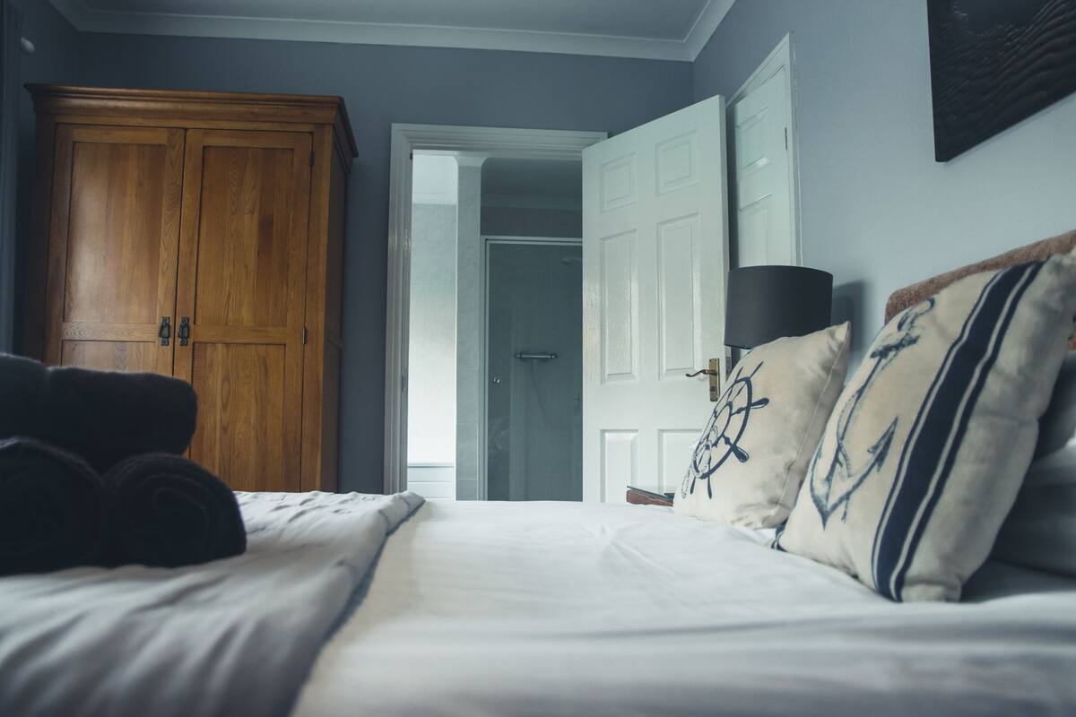 Un dormitorio con un armario de madera, una cama con toallas dobladas y una mesita de noche con una lámpara.