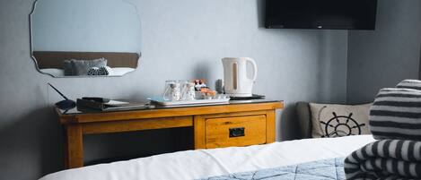 A neatly arranged hotel room with a bed, a bedside table with a kettle, a mirror, and a flat-screen TV on the wall.