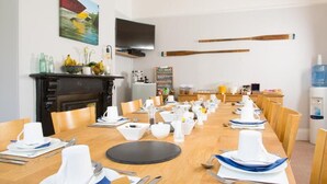 A dining area with a long table set for a meal, a television mounted on the wall, and a fireplace. - Mariners Guest House (Plymouth)