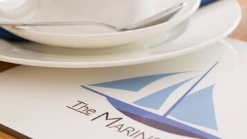 Uma mesa posta com xícara e pires brancos, uma colher e um logotipo com um veleiro.
