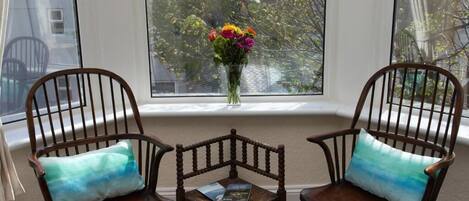 Two wooden chairs with cushions, a small table, and a vase with flowers on a windowsill.