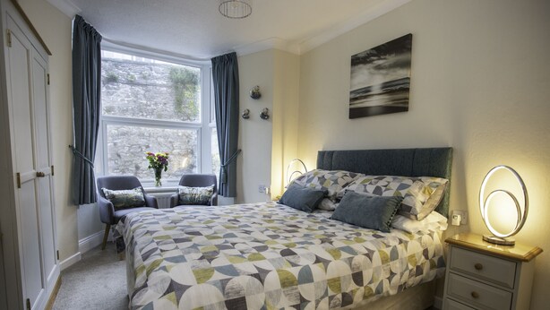 A bedroom with a large bed, bedside tables, a desk, and a window with curtains. - Mariners Guest House (Plymouth)