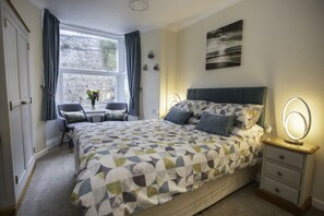 A bedroom with a large bed, bedside tables, a desk, and a window with curtains. - Mariners Guest House (Plymouth)