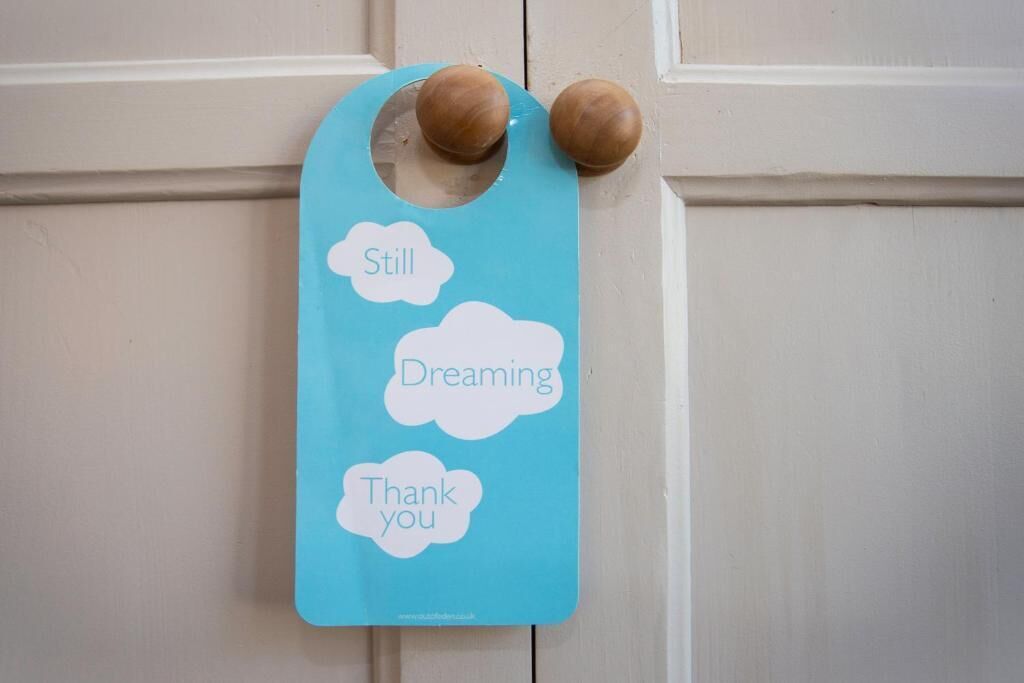Un letrero azul con recortes en forma de nubes que contienen las palabras 'Still', 'Dreaming' y 'Thank you'.