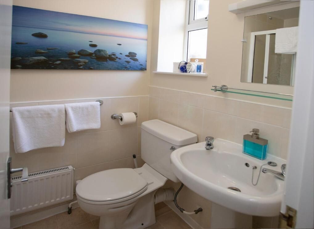 A bathroom with a toilet, sink, and a painting of a beach scene.