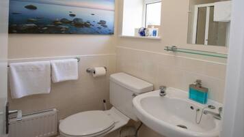 A bathroom with a toilet, sink, and a painting of a beach scene.