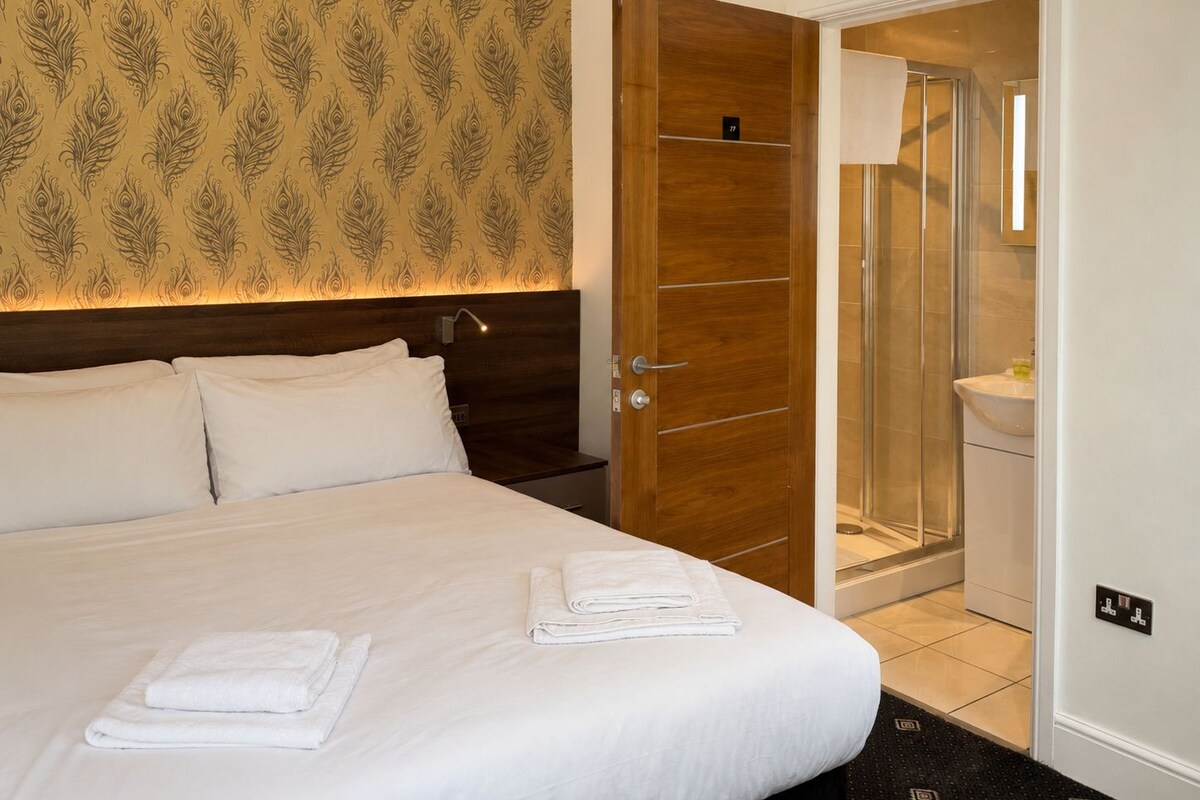 A hotel room with a bed, a wooden door, a shower area, and a bathroom.