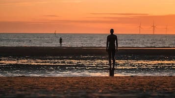 A beach scene with a person standing facing the ocean, with wind turbines in the distance.