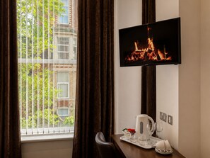 A hotel room with a television displaying a fireplace, a window with curtains, and a table with a kettle and glasses. - Marlborough Hotel (Liverpool)