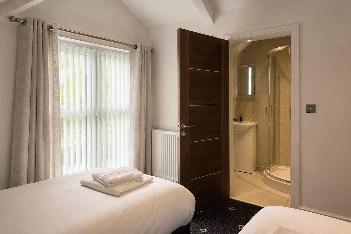A hotel room with a bed, a bathroom with a shower, and a door leading to another room.