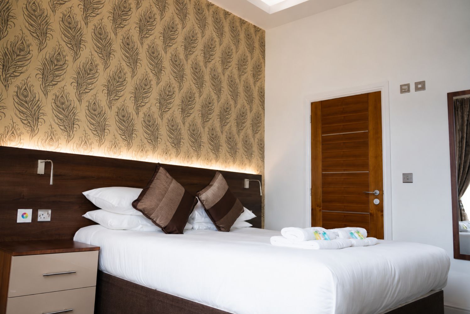 Una habitación de hotel con cama, mesitas de noche, armario y papel tapiz estampado.
