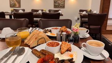 A breakfast setting with plates of eggs, sausages, mushrooms, and toast, along with beverages and a coffee cup.