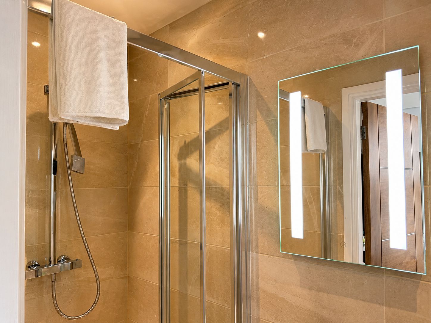 A modern bathroom with a glass-enclosed shower, a large mirror, and a towel hanging on the wall.