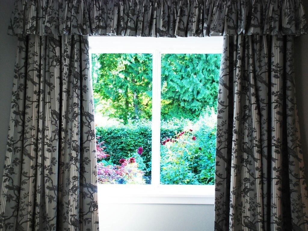 Una ventana con cortinas florales y vistas a un jardín.