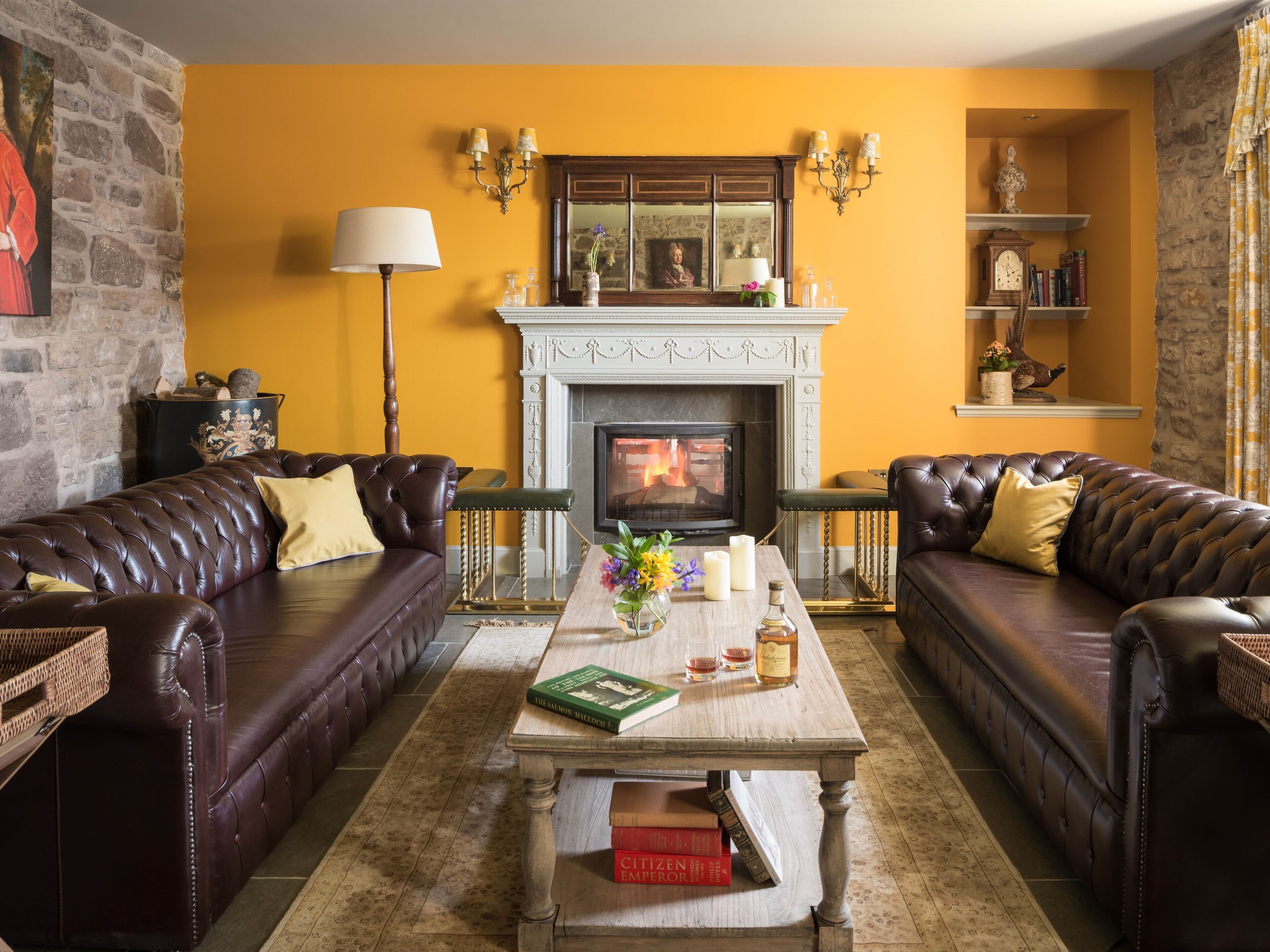 Ein gemütliches Wohnzimmer mit Kamin, Ledersofas, einem Couchtisch mit Büchern und Kerzen sowie einer Steinwand.