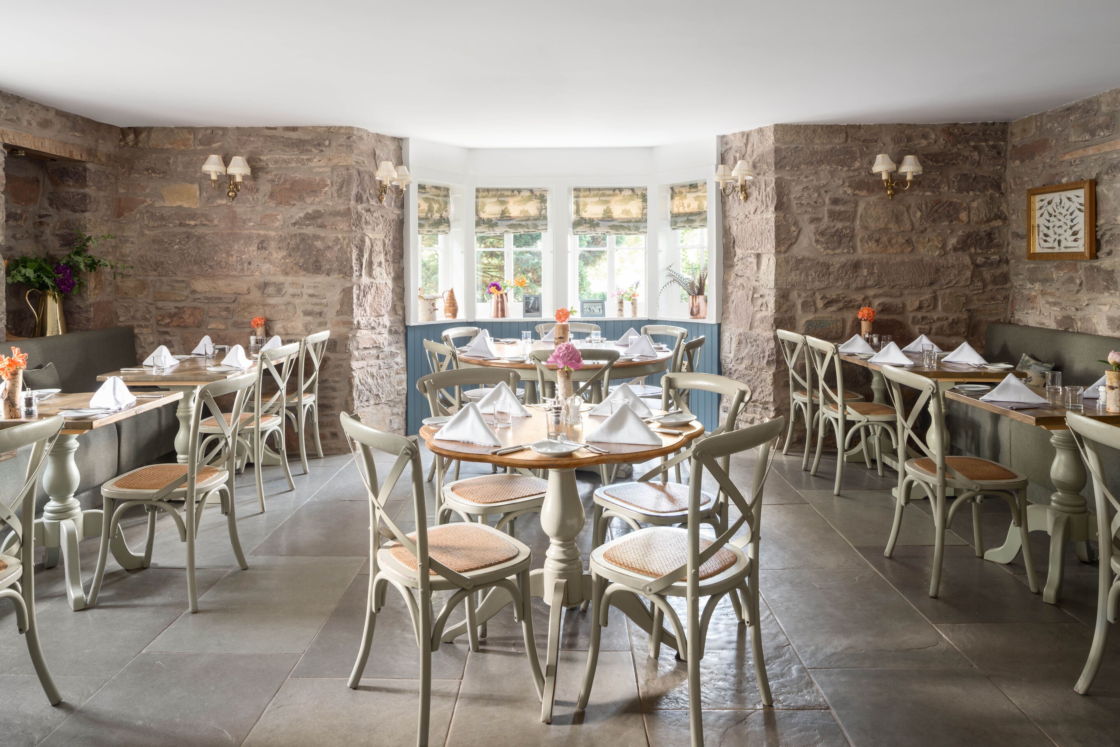 A restaurant with stone walls, round tables, and wicker chairs.